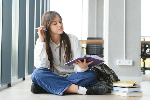 Ragazza sorridente Bella studentessa sorridente mentre era seduto vicino alla finestra e leggendo un libro