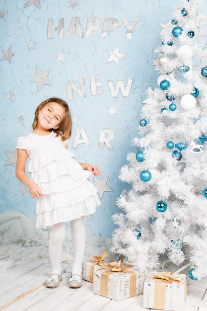 Ragazza sorridente che balla quasi all'albero di Natale con le decorazioni e i regali di Natale