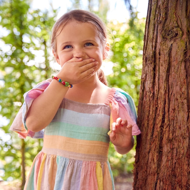 Ragazza sorridente che gioca a nascondino dietro l'albero in giardino