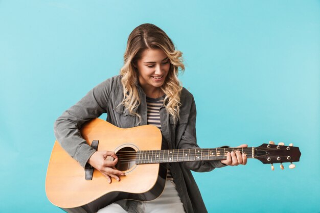 Ragazza sorridente che gioca una chitarra mentre sedendosi isolato sopra l'azzurro