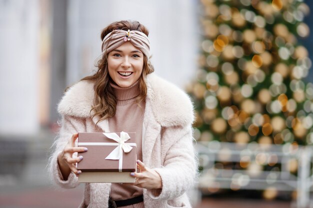 Ragazza sorridente che giudica presente con l'albero di abete decorato vago