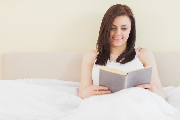 Ragazza sorridente che legge un libro che si trova sul letto