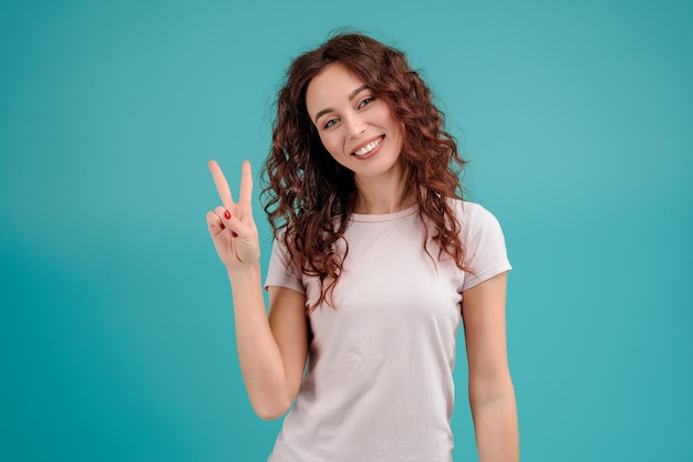 Ragazza sorridente che mostra due dita isolate sopra fondo blu