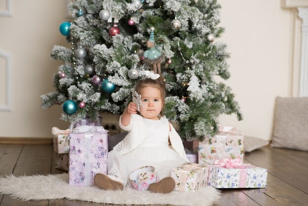 Ragazza sorridente che si siede sotto l'albero e apre i regali di Natale