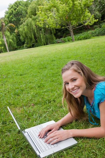 Ragazza sorridente che si trova in un giardino pubblico mentre lavorando al suo computer portatile