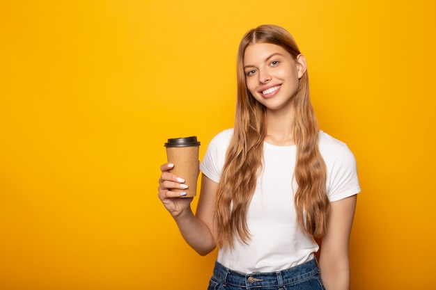 ragazza sorridente che tiene caffè per andare isolato su giallo