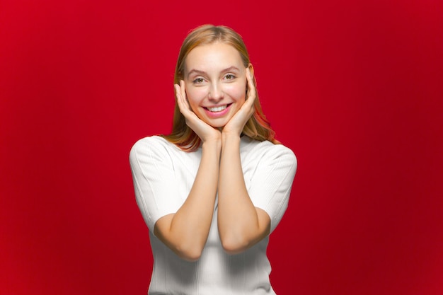 Ragazza sorridente che tocca la pelle liscia perfetta del viso che guarda l'obbiettivo su sfondo rosso per studio