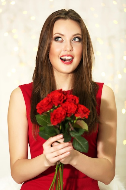 Ragazza sorridente con bouquet di rose rosse su sfondo di luci