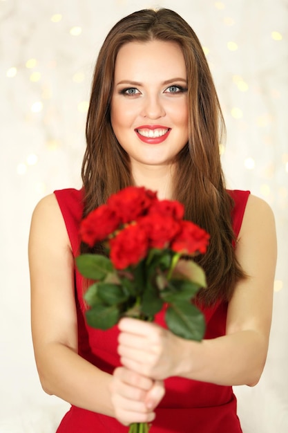 Ragazza sorridente con bouquet di rose rosse su sfondo di luci