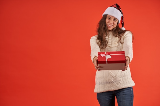 Ragazza sorridente con cappello di babbo natale e regalo in mano su sfondo arancione