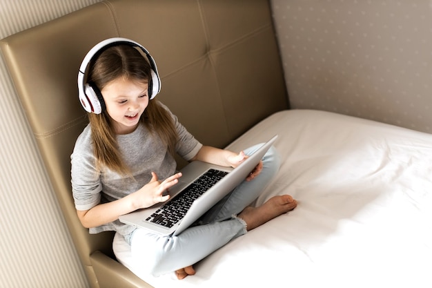 Ragazza sorridente con cuffie wireless usando il suo computer portatile sul letto di casa