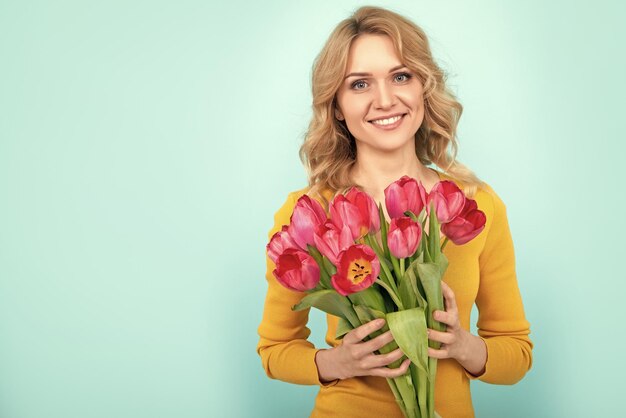 Ragazza sorridente con fiori di tulipano di primavera su sfondo blu