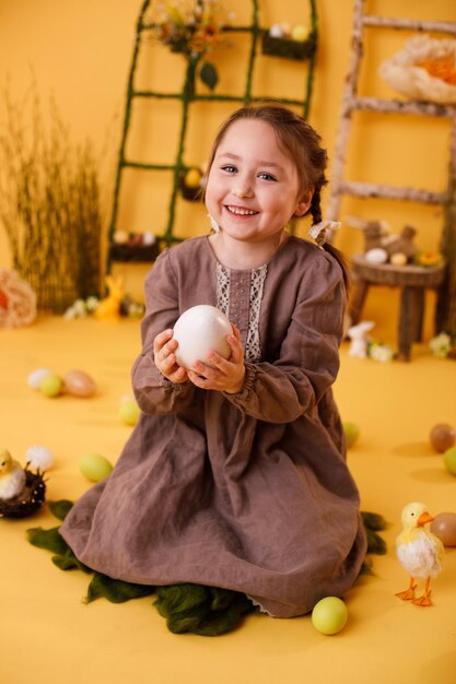 Ragazza sorridente del bambino che gioca con la decorazione tradizionale di pasqua dell'uovo di Pasqua enorme nello stile rurale