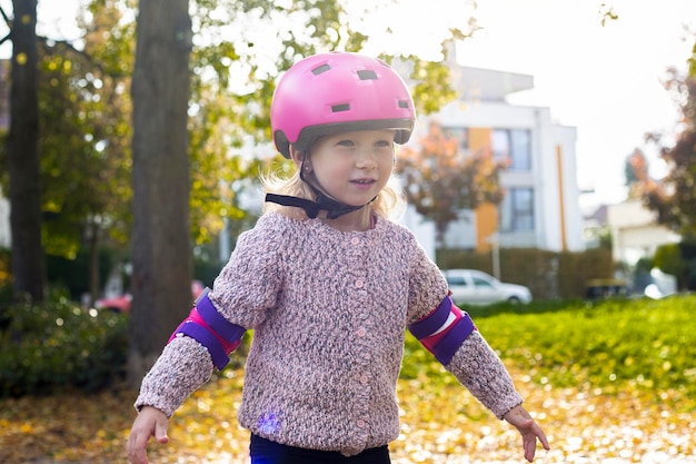 Ragazza sorridente del bambino in un casco in rollerblades di protezione nel parco
