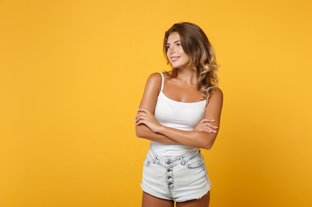 Ragazza sorridente della giovane donna in vestiti casuali leggeri che posano isolata sul fondo giallo arancio della parete, ritratto dello studio. Concetto di stile di vita delle persone. Mock up spazio di copia. Tenendosi per mano incrociata, guardando da parte.