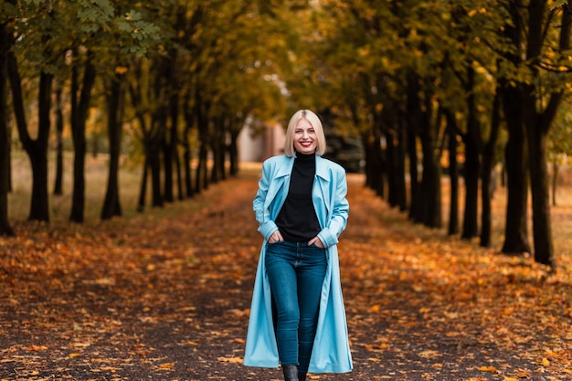 Ragazza sorridente di bellezza felice in abiti alla moda con cappotto, maglione e jeans che camminano nel parco autunnale