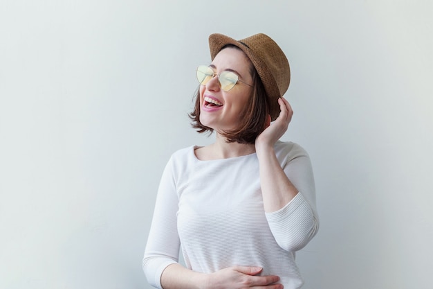 Ragazza sorridente di moda hipster in occhiali da sole gialli alla moda e cappello isolato su bianco