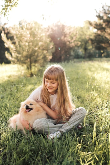 Ragazza sorridente divertente del bambino che gioca con il cane dello spitz che si siede nell'erba verde