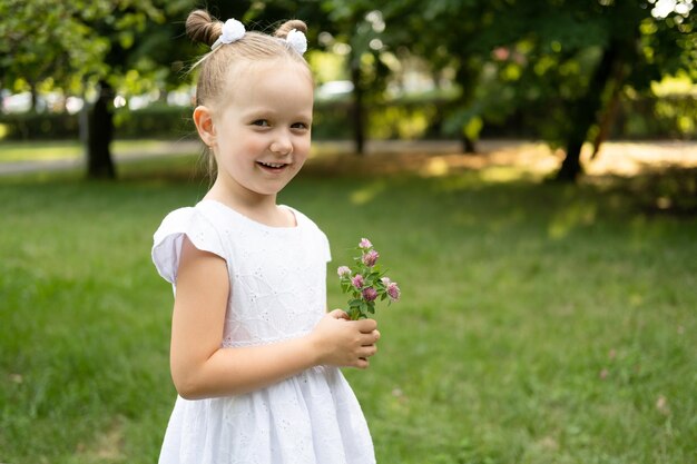 ragazza sorridente divertente del bambino in vestito bianco con i fiori di primavera nel parco verde