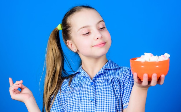 Ragazza sorridente faccia tenere ciotola dolci marshmallow in mano sfondo blu Kid ragazza con i capelli lunghi come mangiare dolci e dolcetti Dolci l'unico vero amore Dolce concetto di dente Calorie e dieta