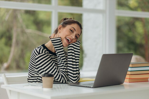 Ragazza sorridente felice che fa lavoro usando il computer portatile a casa