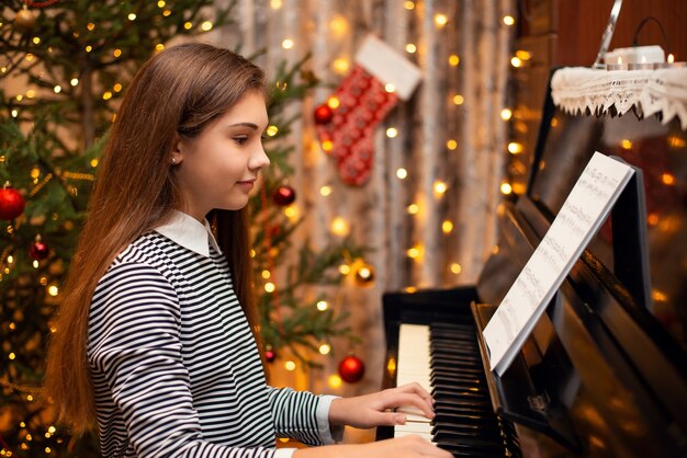Ragazza sorridente felice che gioca il pianoforte con decorazioni luminose sullo sfondo