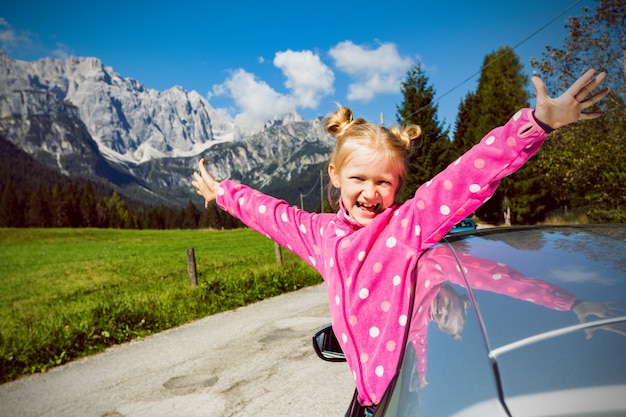 Ragazza sorridente felice che guarda fuori dal finestrino dell'auto e le montagne sullo sfondo. Dolomiti, Italia