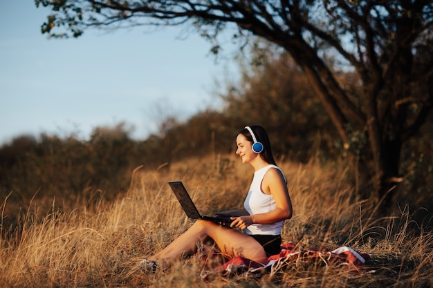 Ragazza sorridente felice che lavora al computer portatile nel parco. Lavora su laptop, concetto di business freelance.