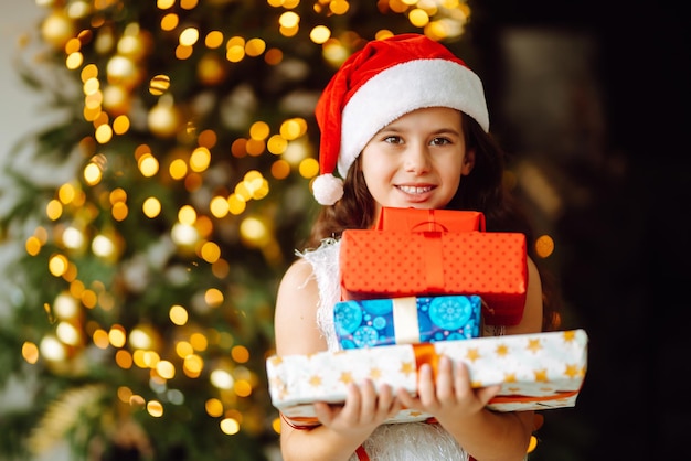 Ragazza sorridente felice con i contenitori di regalo di natale. Cute Child si diverte vicino all'albero.