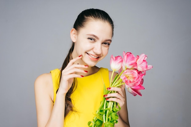 Ragazza sorridente felice in un vestito giallo alla moda che tiene bei fiori rosa di buon umore