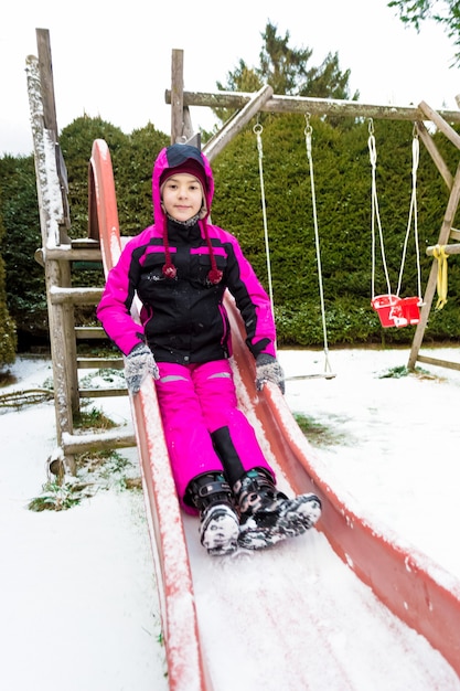 Ragazza sorridente felice sulla diapositiva al freddo giorno di neve