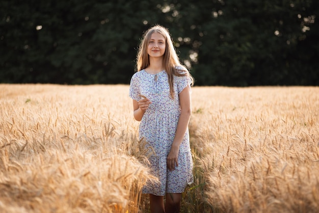 Ragazza sorridente in abito leggero nel campo di grano maturo in possesso di una spighetta Bella ragazza che cammina nel campo di segale matura