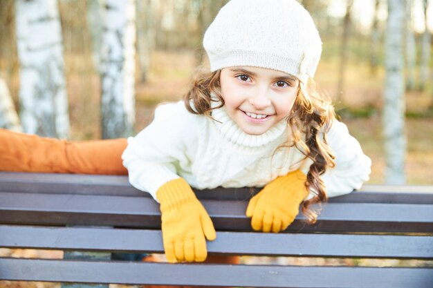 Ragazza sorridente in maglione bianco e berretto nel parco in autunno. Foto di alta qualità