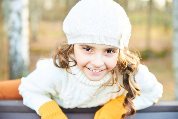 Ragazza sorridente in maglione bianco e berretto nel parco in autunno. Foto di alta qualità