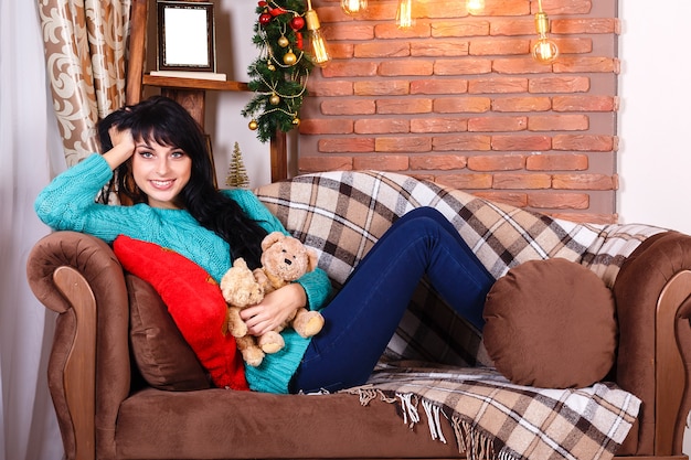 Ragazza sorridente sveglia che si siede sul sofà con la decorazione di natale