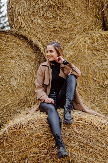 Ragazza sorridente sveglia con il cappello che posa davanti alla balla della paglia del grano