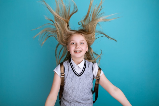 Ragazza sorridente sveglia in un vestito da scuola con lo zaino isolato.