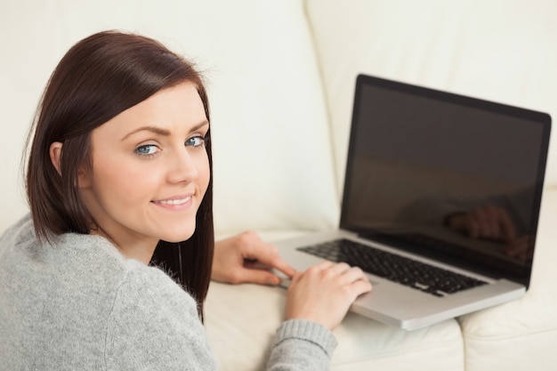 Ragazza sorridente utilizzando un computer portatile su un divano guardando la fotocamera