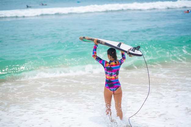 Ragazza sottile sexy con tavola da surf sulla spiaggia di sabbia tropicale. Stile di vita sano e attivo nella vocazione estiva.