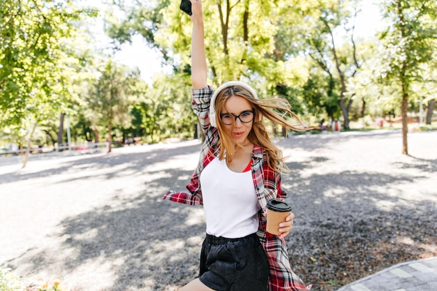 Ragazza spensierata che esprime felicità in estate Giovane signora ben vestita che beve caffè nel parco