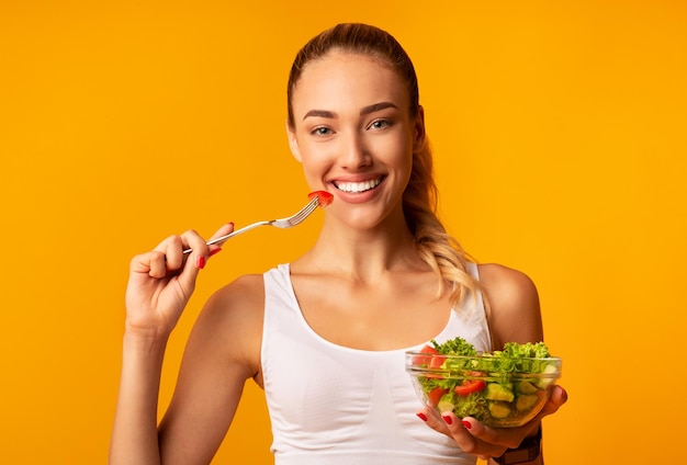 Ragazza sportiva che gode di insalata di verdure in piedi tenendo la ciotola in studio