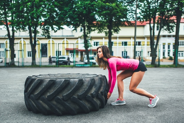 Ragazza sportiva sveglia che solleva gomma enorme all&#39;aperto