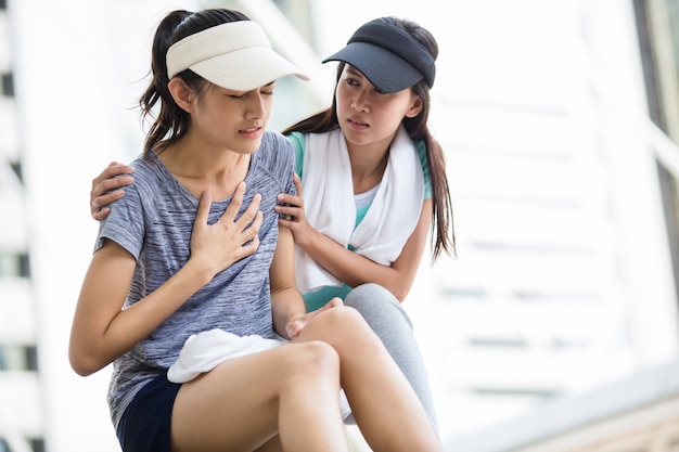 Ragazza sportiva tenta di aiutare la sua amica che ha un mal di cuore mentre fa jogging in città.