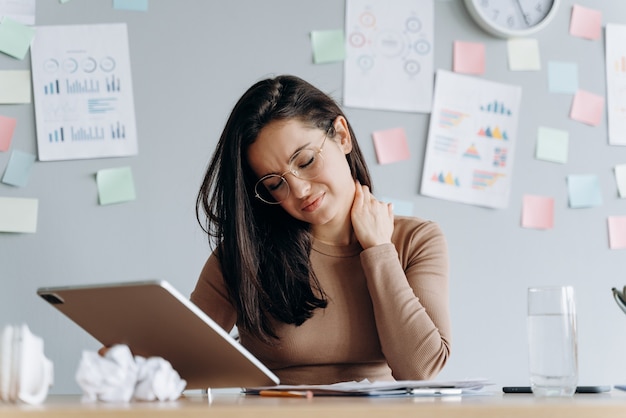 Ragazza stanca per il lungo lavoro sul tablet, si tocca il collo, per la stanchezza chiuse gli occhi