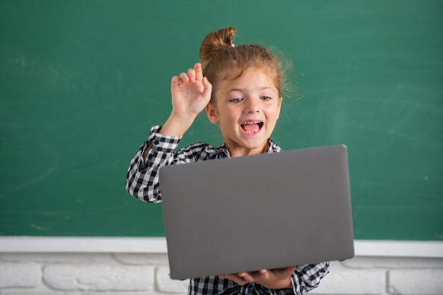 Ragazza studentessa eccitata che utilizza il computer portatile nella classe scolastica sulla lavagna