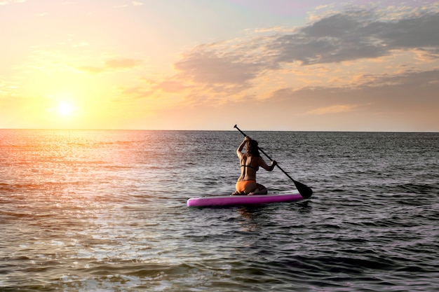 Ragazza su paddleboard sup, mare con caldi colori del tramonto