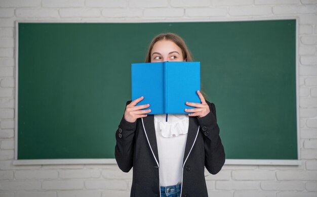 Ragazza su sfondo lavagna che si nasconde dietro la cartella di lavoro a scuola