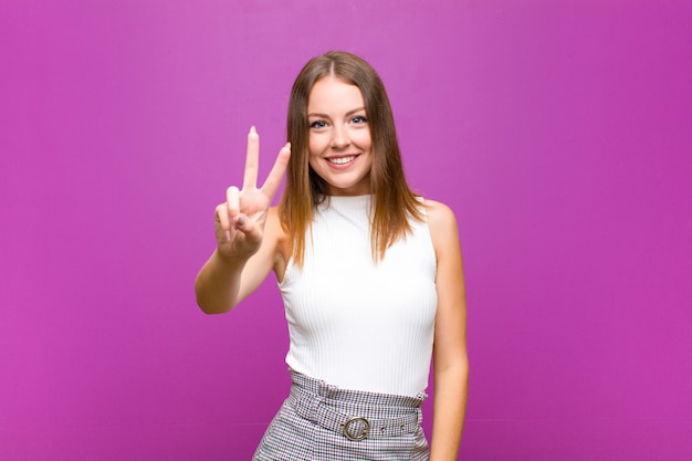 ragazza su sfondo viola sorridendo e guardando felice gesticolando vittoria o pace con una mano