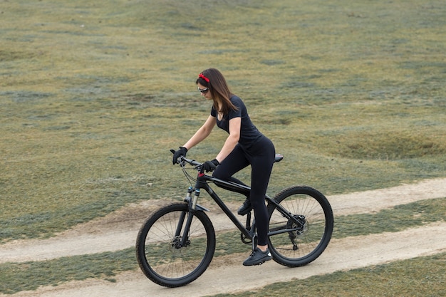 Ragazza su una mountain bike in fuoristrada, bellissimo ritratto di un ciclista in caso di pioggia, Ragazza fitness guida una moderna mountain bike in fibra di carbonio in abbigliamento sportivo. Ritratto del primo piano di una ragazza in bandana rossa.