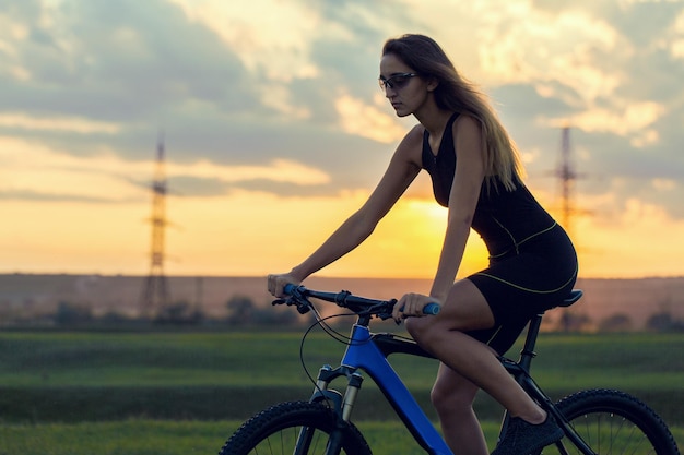 Ragazza su una mountain bike su fuoristrada bellissimo ritratto di un ciclista al tramonto Ragazza fitness cavalca una moderna mountain bike in fibra di carbonio in abbigliamento sportivo